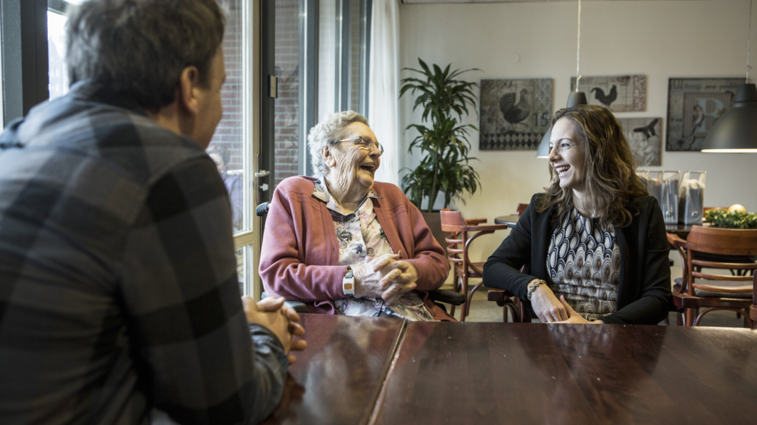 oudere vrouw lacht vrolijk tijdens een gesprek met haar mantelzorger