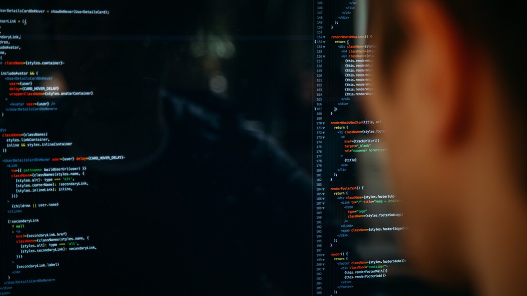 Een computerscherm vol met code, met het zij-aanzicht van een persoon wat naar het beeldscherm kijkt