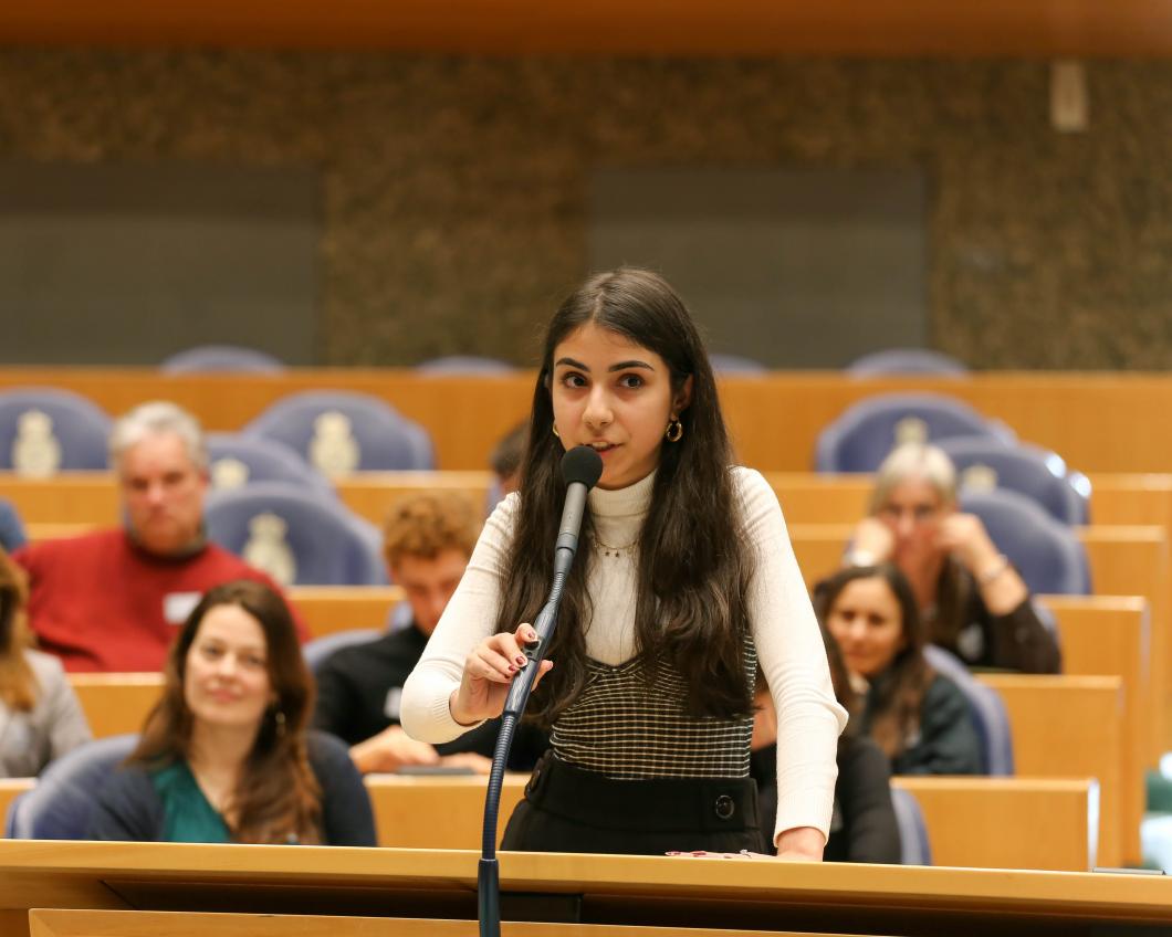 Een jonge bezoeker spreekt andere bezoekers toe achter de interruptiemicrofoon tijdens de actieve ledendag in de Tweede Kamer
